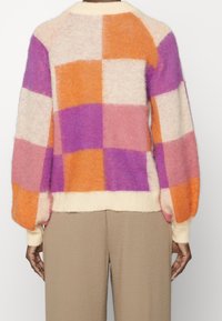 Sweter dziergany z dużymi rękawami, z wzorem patchworkowym w kolorach pomarańczowym, różowym, fioletowym i kremowym. Miękka tekstura i prążkowane mankiety.