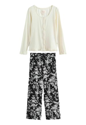 Cremefarbenes Langarm-Oberteil mit Knöpfen und Rüschensaum, kombiniert mit schwarzen, weit geschnittenen Hosen mit weißen Blumenmustern.