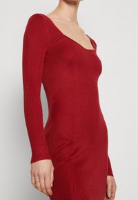 Czerwona sweterkowa sukienka z długimi rękawami i kwadratowym dekoltem. Charakteryzuje się dopasowanym krojem i miękkim, teksturowanym materiałem.