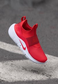 Sneaker slip-on rossa Nike con upper texturizzato, fascia elastica e suola bianca. Presenta un anello frontale e un logo prominente sulla fascia.