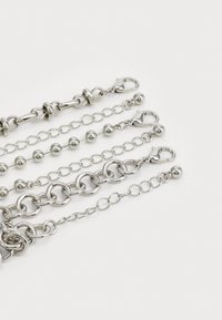 Silver metal chains of varying designs, including circular links, beads, and claw clasps, displayed on a white background.