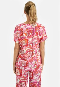 Kolorowa bluzka w kwiatowy wzór i dopasowane spodnie w odcieniach różu, czerwieni i bieli, charakteryzujące się krótkimi rękawami oraz luźnym krojem.