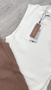 Lähikuva ribbed ilman hihoja paidoista valkoisena ja ruskeana, valkoisessa paidassa on hintalappu, jossa lukee "Luomupuuvilla".