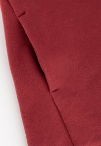 Roter Baumwollstoff mit einer weichen Textur und einem ungesäumten Rand sowie Nähten. Das Material ist leicht und glatt.