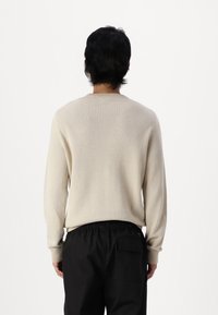 Beige gebreid trui met een gestructureerd patroon, ronde hals en geribbelde mouwen, gecombineerd met zwarte broeken met een elastische tailleband.