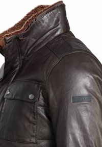 Bruine leren jas met een gestructureerde afwerking, een met bont gevoerde kraag en een klein logo-label op de schouder. Voorzien van drukknoopzakken.