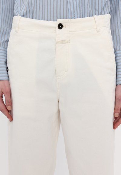 White denim pants with a straight cut, featuring a black button and a subtle logo tag on the waistband. Texture appears smooth and sturdy.