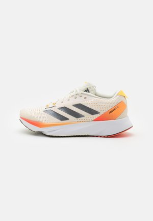 Zapatilla de running ligera en color crema con detalles en naranja y rayas negras. Cuenta con una parte superior de malla transpirable y una suela acolchada para mayor comodidad.