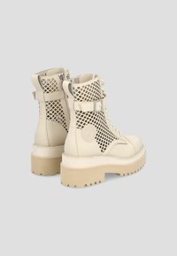Bottines beiges à lacets avec semelles épaisses, panneaux en maille ajourée sur les côtés, fermetures éclair latérales et brides à boucle autour de la cheville.