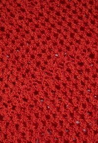 Tessuto a maglia rossa con un motivo aperto e arioso, caratterizzato da un filato testurizzato e intricati anelli che creano un materiale leggero e traspirante.