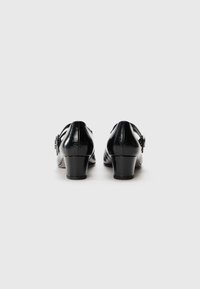 Chaussures noires en cuir à talon avec une finition brillante. Elles présentent un petit talon épais et une boucle décorative sur le côté pour l'accent.