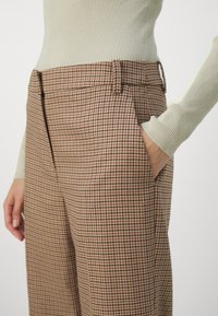 Pantaloni a quadri marroni con una vestibilità sartoriale, dotati di tasche laterali, una texture liscia e un design a vita alta.