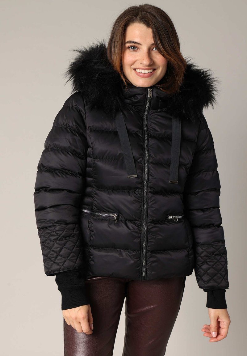 Doudoune noire avec une capuche en fausse fourrure, fermeture éclair à l'avant et poches, panneaux texturés et poignets élastiqués. Fabriquée en tissu durable et brillant.
