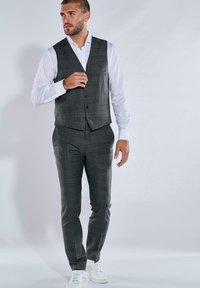 Grauer kariertes Dreiteiler-Anzug bestehend aus Weste, Hose und weißem Hemd, kombiniert mit weißen Sneakers. Maßgeschneiderte Passform, minimalistisches Design.