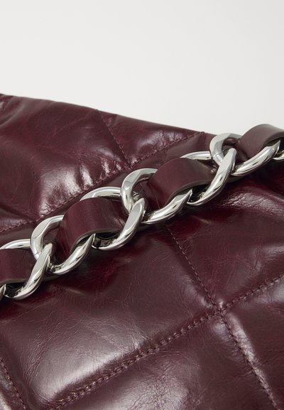 Bordo usnjeni ročni torbici s prešito zasnovo, ki ima srebrno verižico in gladko teksturo. Izstopa po svoji bogati barvi in strojni opremi.
