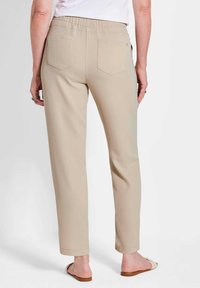 Beige elastische taillebandbroek met een rechte pijp, twee achterzakken en opgerolde omslagen. Gladde stoftextuur, gestyled zonder zichtbare sluitingen.