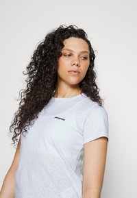 White short-sleeve T-shirt with a round neck and a black Patagonia logo on the chest, made from a soft, textured cotton fabric.