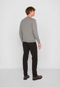 Grauer Strickpullover mit langen Ärmeln, rundem Hals und geripptem Saum, kombiniert mit schwarzen Slim-Fit-Hosen und grauen Ankle-Boots.