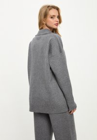 Šedý pletený svetr s ohnutým límcem, oversized střih, žebrované manžety a spodní lem, doplněný o odpovídající šedé kalhoty z měkkého materiálu.
