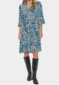 Blå och svart leopardmönstrad klänning med v-ringning, tre fjärdedels ärmar och lagerkjol, parat med knähöga svarta stövlar.