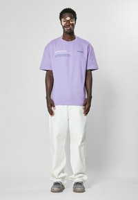 Purple cotton t-shirt with short sleeves, printed text; paired with white relaxed-fit pants and gray sneakers. Smooth texture throughout.