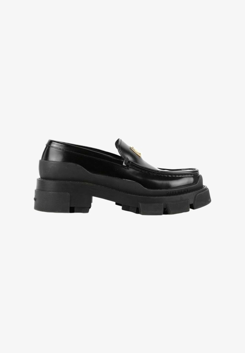 Mocassin en cuir noir avec une semelle épaisse et robuste et un emblème décoratif doré sur le dessus, montré de profil sur fond blanc.