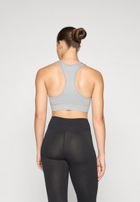 Lys grå sportsbh med racerback-design, laget av et stretchy materiale. Kombinert med høy midje svarte leggings, med en glatt tekstur.