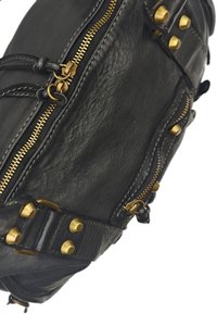 Sac à main en cuir noir avec fermetures éclair dorées, clous décoratifs et coutures détaillées. Design en courbe avec plusieurs compartiments et textures.