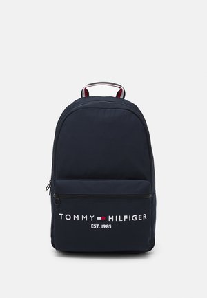 Mochila Tommy Hilfiger azul marino con bolsillo delantero con cremallera, logo y texto "EST. 1985", con detalle en el asa en rojo, blanco y azul.