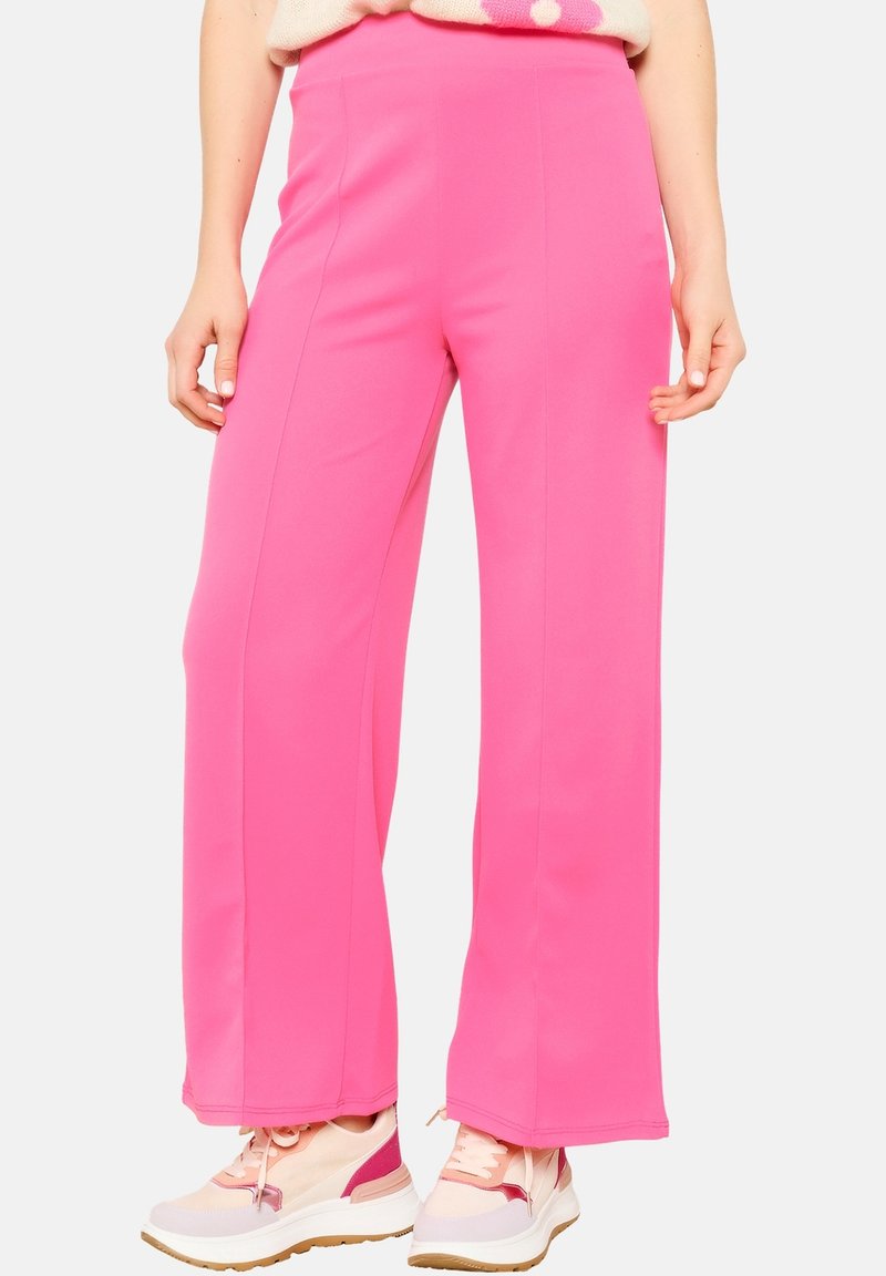 Pantalons larges rose vif en tissu lisse et extensible. Dotés d'une taille haute et de coutures nettes. Portés avec des baskets de couleur neutre.