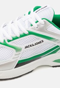 Hvit mesh-sneaker med grønne detaljer, sølvfarge og svart såle. Har hvite snørebånd og merkevarenavnet "Jack & Jones" på siden.