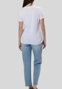 Camiseta blanca de manga corta con cuello redondo, combinada con jeans rectos de color azul claro con dobladillos deshilachados.