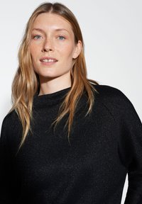 Pull noir étincelant avec col montant, texture douce et coupe ample. Présente un design de manche raglan et un léger scintillement sur l'ensemble.