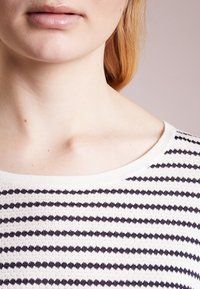 Roomkleurige trui met marineblauwe horizontale strepen, gebreide textuur, brede halslijn en een licht losse pasvorm rond de schouders.