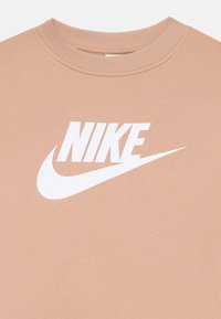Persikinės spalvos Nike džemperis su dideliu baltu Nike logotipu priekyje, apvaliu kaklu ir raukiniais ant rankovių. Minkšta medžiagos tekstūra.