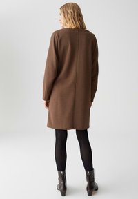 Bruine gebreide jurk met een losse pasvorm, lange mouwen, een achternaad detail, gecombineerd met zwarte maillots en laarzen met rits bij de enkels.