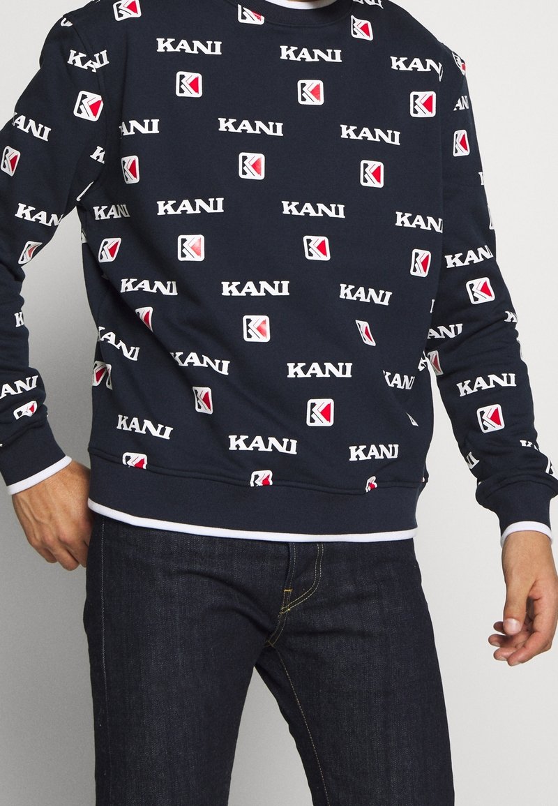 Felpa blu marina con un motivo ripetuto del logo KANI in bianco e rosso. Collo a giro, polsini a coste e finitura in tessuto testurizzato.