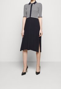 Abito a righe navy e bianche con collo polo, maniche corte, chiusura frontale con bottoni e spacchi laterali, realizzato in una maglia testurizzata.