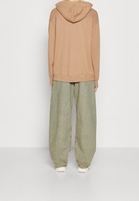 Brown hoodie with a drawstring, paired with oversized light green denim pants. Features relaxed fit and visible stitching details.