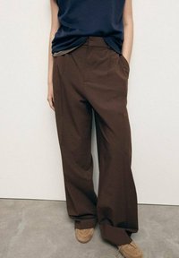 Bruine wijde broek met een hoge taille en zakken aan de voorkant, gemaakt van een gladde stof. Gecombineerd met een marineblauw mouwloos topje en beige schoenen.