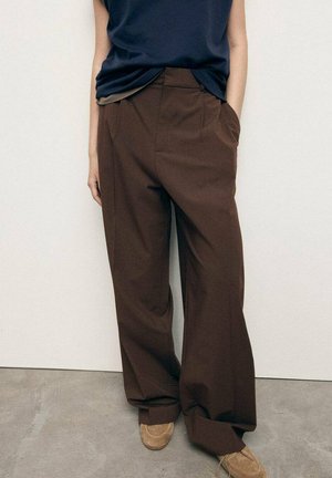 Brown wide-leg trousers with a high waist and front pockets, made of a smooth fabric. Paired with a navy sleeveless top and beige shoes.