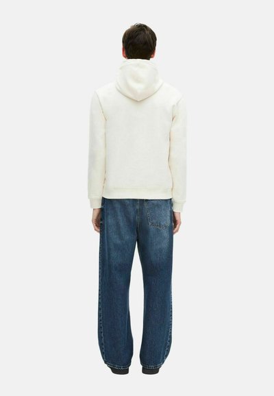 Beige Kapuzenpullover mit lockerer Passform, kombiniert mit lockeren blauen Jeans aus Denim, die eine Gesäßtasche und weite Beine haben.