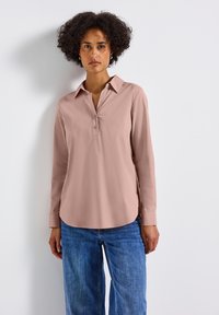 Camicia button-up rosa chiaro a maniche lunghe con colletto e orlo curvo, realizzata in tessuto morbido. Abbinata a jeans blu a gamba larga.