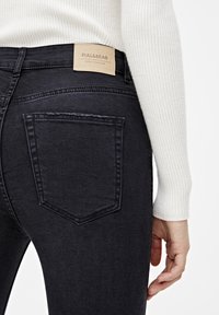 Jeans de mezclilla negra con un diseño ajustado, que cuentan con un bolsillo trasero y una etiqueta beige de Pull&Bear en la cintura. Textura suave, detalles mínimos.
