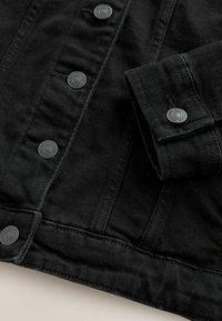 Zwarte denim jack met een knoopsluiting aan de voorkant, metalen knopen en een gestructureerde pasvorm. De stof heeft een textuur met zichtbare stiksels.