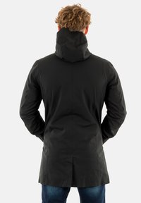 Manteau noir imperméable avec capuche, design long, texture lisse et coupe droite, présentant des coutures décoratives et une fente au dos.