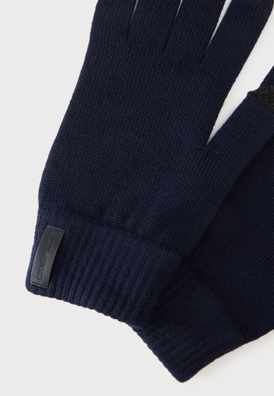 Paire de gants tricotés bleu foncé avec poignets côtelés et petite étiquette noire rectangulaire sur un poignet.