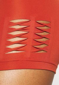 Červené atletické kraťasy s řadou výřezů po stranách, které předvádějí hladkou, pružnou látku se štíhlým designem.