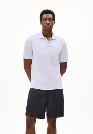 Weißes Polohemd mit Kragen und kurzen Ärmeln, kombiniert mit dunkelblauen Shorts. Einfaches Design, glattes Material und dezente Logodetails.