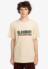 Beige bomulds T-shirt med iøjnefaldende grøn "ELEMENT" og rød tekst. Enkel, løs pasform med korte ærmer og rund halsudskæring.